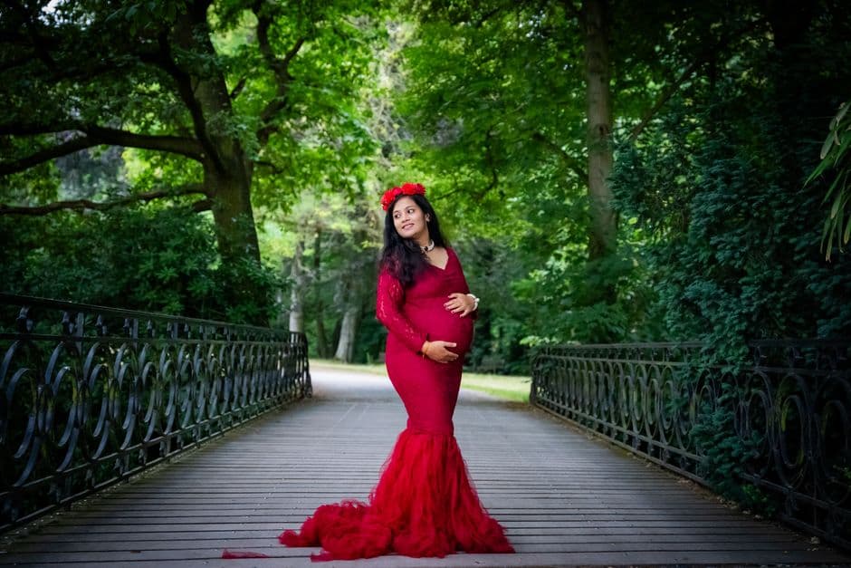A woman in a red dress poses on a footbridge surrounded by forest greenery.