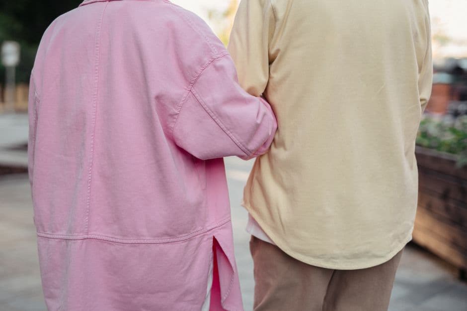 A couple in pink and yellow jackets walking outdoors, showcasing affection and romance.