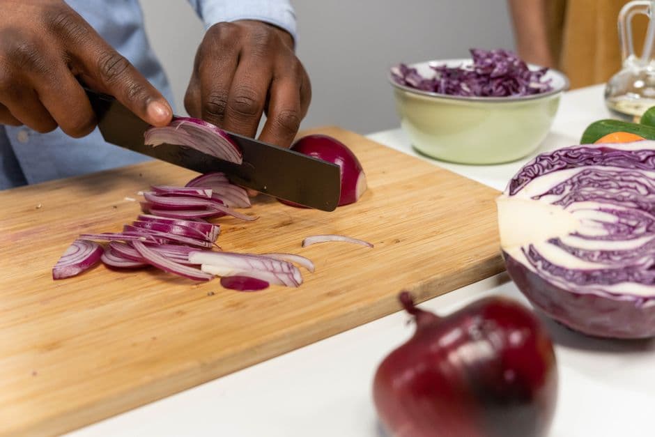 Close-up of hands slicing red onions on a wooden chopping board in a kitchen setting.