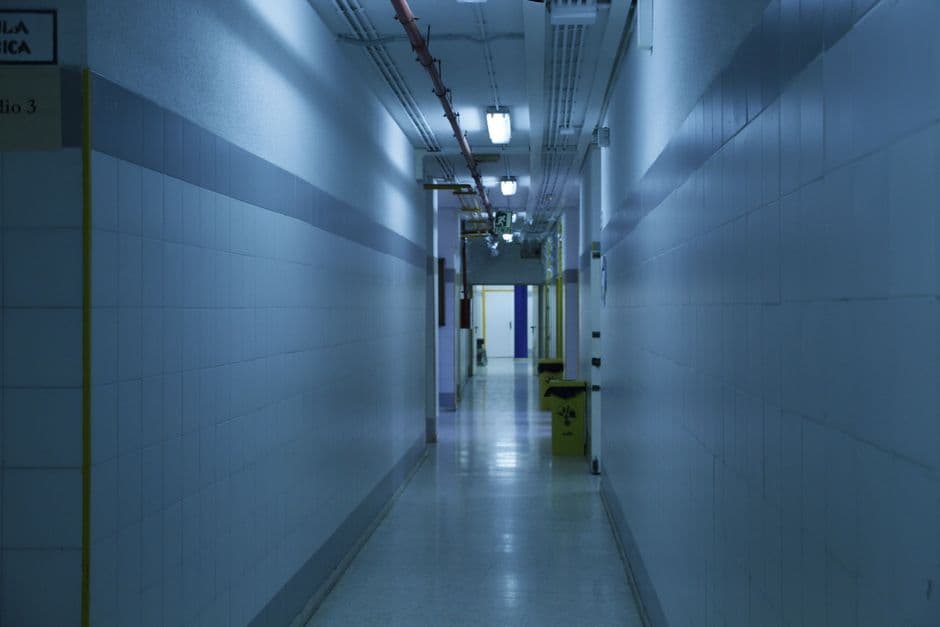 A deserted, dimly lit hallway with tiled walls and overhead lights.
