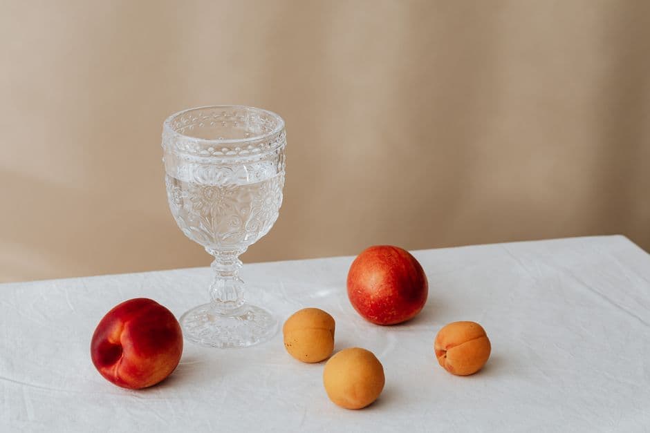 Crystal glass filled with water, accompanied by peaches and apricots on a white tablecloth, creating an elegant still life composition.