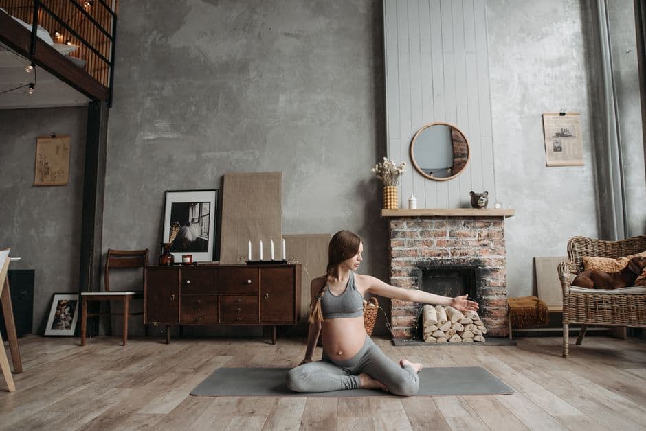 Pregnant woman practicing yoga in a cozy living room with her pet dog nearby.