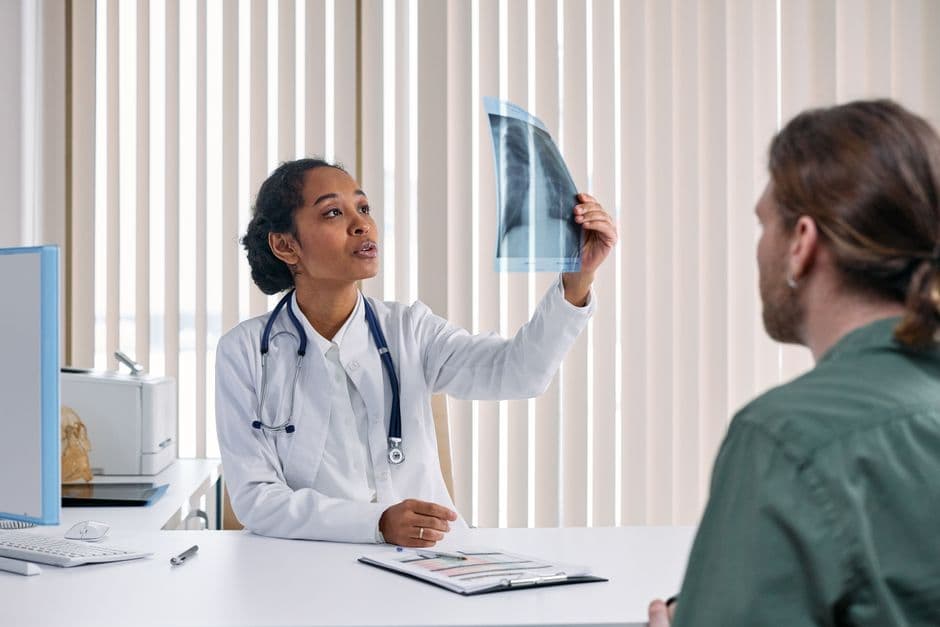 Female doctor examines x-ray results with male patient in a medical setting.