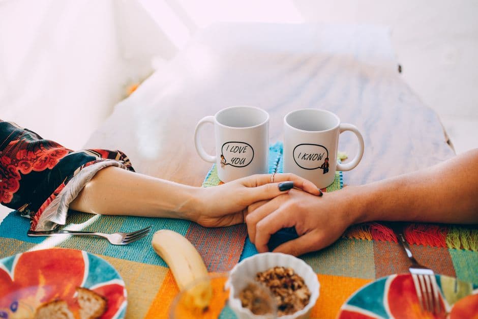 A cozy breakfast scene with two mugs, holding hands, and a colorful table setting.