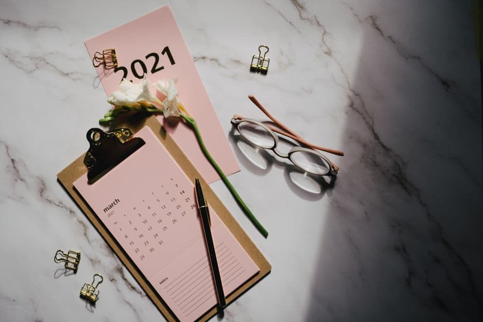 Elegant flat lay featuring a 2021 calendar, glasses, and white flowers on marble surface.
