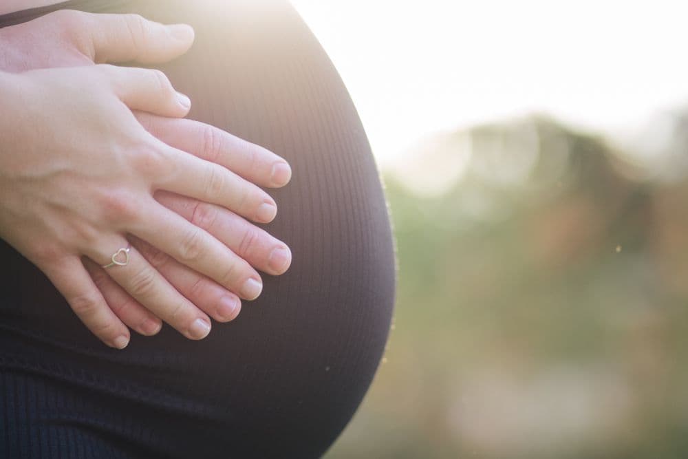 Two hands resting on a pregnant belly, backlit by evening sun