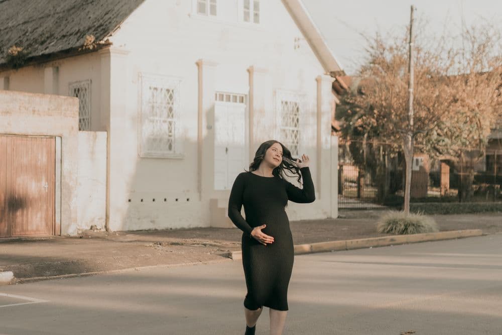 A pregnant woman walking along a quiet street in low golden sunlight