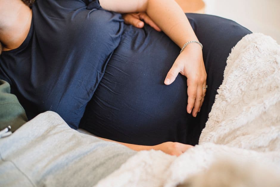 Crop anonymous man embracing expectant woman in home wear while resting in bed at home