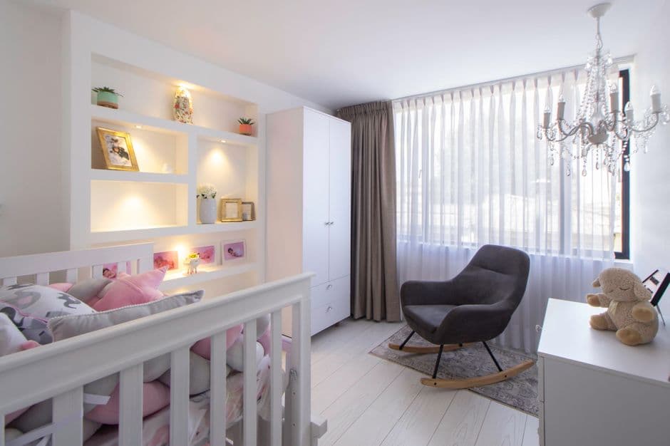 A bright and modern children's room with a crib, armchair, and chandelier.